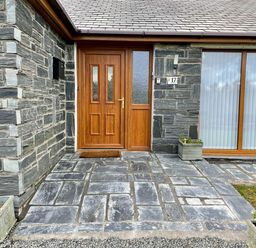 A stone front entrance with a wooden door two planters and a large window at Yr Encil in Llanddaniel near Gaerwen