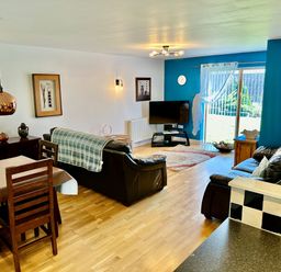 A living room with leather sofas wooden dining table and chairs a corner TV and sliding glass doors at Yr Encil in Llanddaniel near Gaerwen