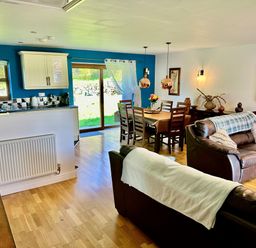 An open plan living room and kitchen with leather sofas a dining table and glass sliding doors at Yr Encil in Llanddaniel near Gaerwen