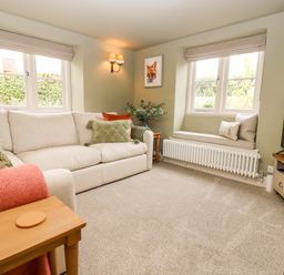 A living room with a beige sofa green cushions window bench with cushions a wall light and a television at 4 Lower Folley in Chipping Campden