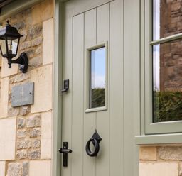 A green door with a black door knocker and handle next to a stone wall with a lantern and a plaque that reads 4 Lower Folley at 4 Lower Folley in Chipping Campden