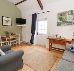 A living room with two sofas a wooden table with chairs a wall-mounted tv and a door at Carreg Cennen Cottage in Llandeilo