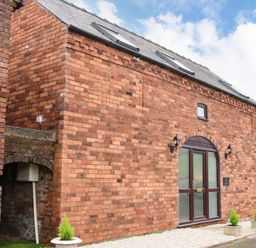 A brick building with an arched glass door and small planters outside at The Little Beehive in Abberley