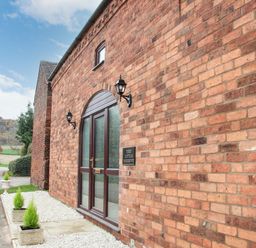 Exterior of a brick building with glass double doors and potted plants at The Little Beehive in Abberley
