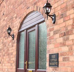 A brick wall with two lamps and an arched door with frosted glass at The Little Beehive in Abberley