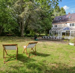 A garden with two deck chairs trees a long table and chairs and a white house with a conservatory at The Firs in Wendling near Dereham