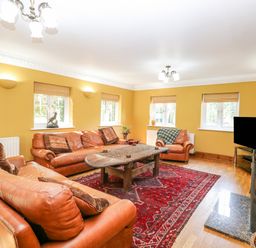 A living room with leather sofas a wooden coffee table a red rug and a television at The Firs in Wendling near Dereham