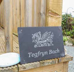 A black slate sign with a dragon illustration and Tegfryn Bach text on a wooden deck at Tegfryn Bach in Llangoed near Beaumaris