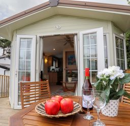 A wooden deck table with apples a wine bottle glasses and a flower pot outside of a building with open double doors at Tegfryn Bach in Llangoed near Beaumaris