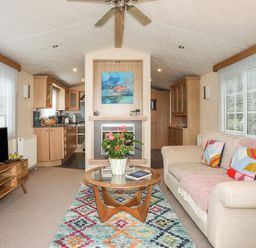 A living room with a beige sofa cushions a glass coffee table plant a flat screen tv a wooden cabinet and a colorful rug at Tegfryn Bach Llangoed near Beaumaris