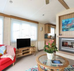 A living room with a red armchair a television on a wooden stand a fireplace and a glass coffee table with a plant at Tegfryn Bach Llangoed near Beaumaris