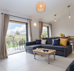A living room with a gray sectional sofa a wooden coffee table and a dining table with chairs at Woodpecker Lodge in Butterleigh