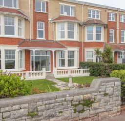 A row of brick houses with bay windows and front gardens behind a stone wall at Weymouth Bay Apartment A Weymouth