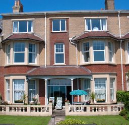 A brick house with bay windows a small patio and garden with flowers at Weymouth Bay Apartment A Weymouth