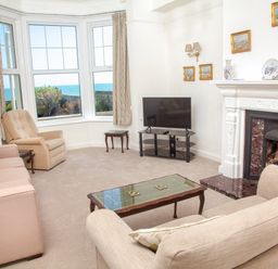 A living room with sofas an armchair a glass coffee table a television and a fireplace with paintings on the wall at Weymouth Bay Apartment A Weymouth