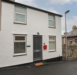 A white two-story house with four windows a gray door and a red mailbox on a street at Clydfan in Caernarfon