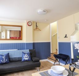 A living room with a black sofa blue cushions and a staircase at Clydfan in Caernarfon