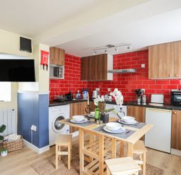 A kitchen with wooden cabinets red tiled backsplash dining table with chairs and a wall mounted television at Clydfan in Caernarfon