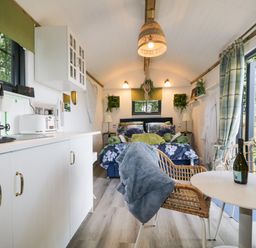A small living space with a bed at the end a kitchen area on the left and a small round table with chairs on the right at High Rigg Shepherd's Sunset in Brampton Cumbria