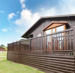 A wooden cabin with a fenced porch in a grassy area at Badgers Retreat in Tunstall near Hipswell