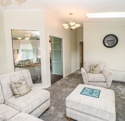 A living room with two armchairs and a sofa with cushions a square ottoman with a board game and a clock on the wall at Badgers Retreat in Tunstall near Hipswell