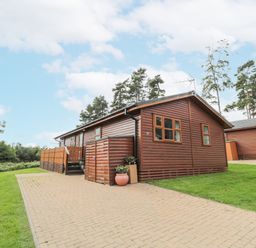 A wooden cabin with a paved driveway and surrounding grass at Hillside View in Alnwick