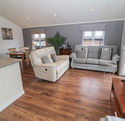 A living area with two sofas a wooden dining table and chairs a television on a wooden stand and windows at Hillside View in Alnwick