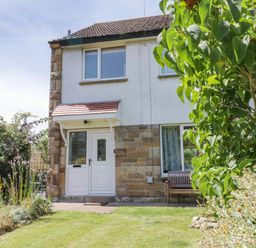A front view of a two-story house with a garden and bench at Sea Change in Newholm near Whitby