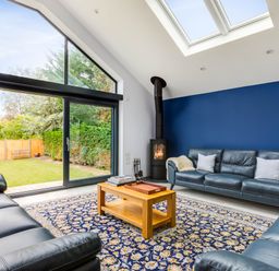 A living room with leather sofas a wooden coffee table a patterned rug a wood-burning stove and large sliding glass doors at The Garden House in Rock