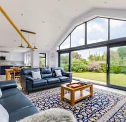A living room with blue leather sofas and a wooden coffee table on a patterned rug next to large glass sliding doors with garden views at The Garden House in Rock