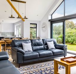 A living room with leather sofas a wooden coffee table rug and large windows showing a garden at The Garden House in Rock
