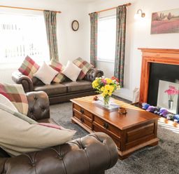 A living room with leather sofas a wooden coffee table with flowers and a fireplace at Gwersyllt in Benllech