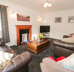 A living room with leather sofas a wooden coffee table a television and a fireplace at Gwersyllt in Benllech
