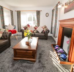 A living room with two leather sofas a wooden coffee table flowers on the table and a fireplace in Gwersyllt Benllech