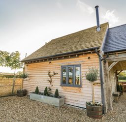 An exterior view of a wooden house with a stone wall and potted plants at The Hyde in Armscote near Newbold on Stour
