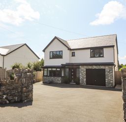 A detached house with a stone wall and driveway at Berllan in Llanbedrgoch near Benllech