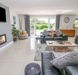 A living room with leather sofas a fireplace a coffee table and sliding glass doors at Berllan in Llanbedrgoch near Benllech