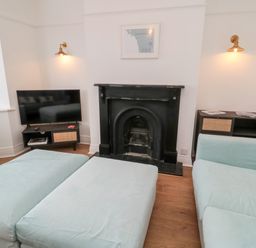 A living room with a light blue sofa and ottoman a black fireplace a television on a stand and wall lights at Shileen in Seahouses