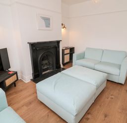 A living room with two light blue sofas a large ottoman a black fireplace a TV on a dark wooden stand and wooden flooring at Shileen in Seahouses