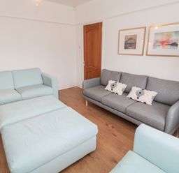 A living room with a grey sofa with cushions a light blue armchair and ottoman wooden floor and framed pictures on the wall at Shileen in Seahouses