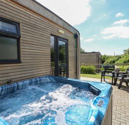 An outdoor hot tub next to a wooden cabin with chairs and a table on a paved patio at Amarone Seaview
