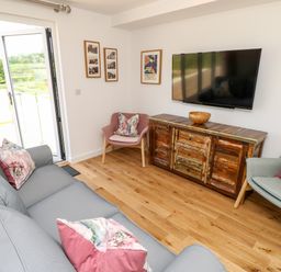 A living room with a gray sofa and floral cushions two armchairs a wooden TV stand with a bowl and a wall-mounted TV at Champagne Seaview