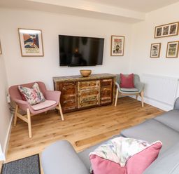 A living room with a wall-mounted TV above a wooden cabinet and three chairs with cushions at Champagne in Seaview