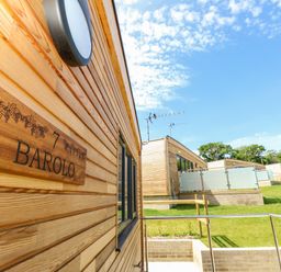 A wooden exterior wall with a Barolo sign and neighbouring wooden lodges on a grassy slope at Barolo in Seaview