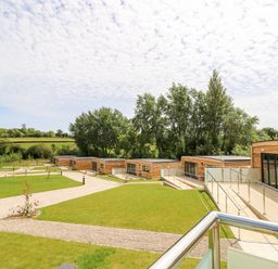 A group of wooden cabins with glass doors and railings surrounded by grass and pathways with trees in the background at Barolo in Seaview