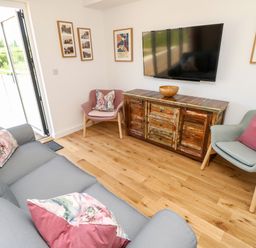 A living room with a grey sofa and floral cushions two armchairs a wooden cabinet with a bowl and a wall-mounted television at Barolo in Seaview