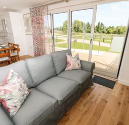 A living room with a gray sofa and floral cushions near sliding glass doors opening to a wooden deck and green lawn at Barolo in Seaview