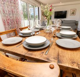 A wooden dining table set with plates, bowls, wine glasses, and cutlery with chairs around it in a dining room at Cava in Seaview