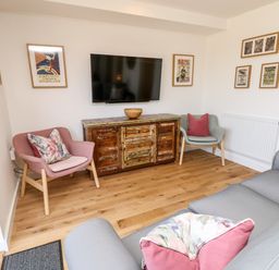 A living room with two armchairs a wooden cabinet under a wall-mounted TV and framed pictures on the wall at Chianti in Seaview