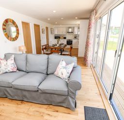 A living area with a gray sofa and floral pillows next to a dining table and kitchen with wooden doors and large sliding glass doors at Chianti in Seaview